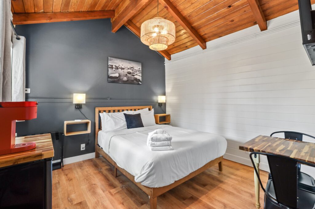 Queen bed against a charcoal wall under a pine ceiling, with a coffee maker and a table for two at Tahoe Mountain Inn